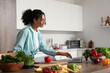 © Pixel-Shot - Young happy African-American woman with laptop and ingredients for fresh salad in kitchen