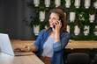 © wavebreak3 - 30s woman wearing denim shirt sitting at coworking counter, holding smartphone and using laptop