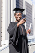 © wavebreak3 - African American woman graduate posing on steps in black gown cap taking phone selfie with diploma