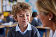 © AI_images - schoolboy crying in classroom while teacher gently speaking to him, bright educational setting, natural daylight, authentic school environment, balanced composition