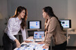 © Tj - Young Asian businesswomen collaborating on a late-night project, discussing financial reports and data charts spread across a table in a modern corporate office