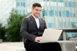 © muse studio - Businessman working on laptop outside modern building during daytime