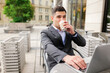 © muse studio - Man sits at outdoor table working on laptop while drinking coffee in the city during daytime