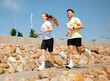 © muse studio - Couple runs together on a sunny day along a rocky path near a city park