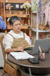 © Ekkasit A Siam - Asian senior florist woman checking accounting notes with serious expression while working on laptop at flower shop showing financial stress from managing small business inventory issues