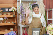 © Ekkasit A Siam - Asian senior female florist enjoying warm tea while standing beside flowers in cozy flower shop during peaceful break surrounded by blooming bouquets and greenery in relaxing workspace