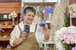 © Ekkasit A Siam - Asian senior female florist wearing apron holding credit card and payment terminal smiling behind flower shop counter representing small flower business accepting cashless payment