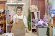 © Ekkasit A Siam - Asian elderly florist standing confidently behind shop counter giving thumbs up while smiling proudly with blooming flowers laptop and digital devices showing trust in online business growth