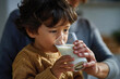 © Milos - A young boy savors milk from a glass, representing the innocent pleasures of childhood and the simple joys found in everyday moments with the warm presence of a nurturing figure.