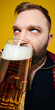 © master1305 - Bearded man drinking large glass of beer close up portrait against yellow background. Concept of beverage campaign, bar menu visuals, seasonal promotion, and hospitality advertising.