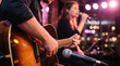 © tonstock - Close up of a musician playing acoustic guitar during a live performance with a female singer on stage.