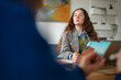 © Studio Marmellata - A young woman with curly hair, wearing a blazer and vest, is engaged in a discussion while looking at a tablet and holding a pencil.