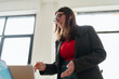© Studio Marmellata - A young woman in glasses and a blazer smiles while holding a pencil and looking at a laptop.