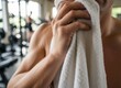 © Rina - Man Wipes Sweat With White Towel After Intense Workout In Gym With Blurred Background Showing Exercise Equipment