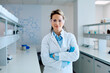 © we.bond.creations - Smiling woman scientist wearing safety goggles, lab coat, and gloves, standing confidently in a modern research laboratory