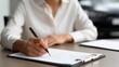 © Mary - Young woman writing notes on clipboard at desk in office environment