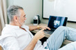 © Daniel Gonzalez/Stocksy - Senior man relaxing in hotel room using laptop
