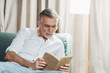 © Daniel Gonzalez/Stocksy - Senior man relaxing reading book on hotel sofa