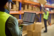 © Studio Romantic - Warehouse inventory worker with laptop near shelves. Staff updates stocktaking data as a colleague moves boxes ensuring storage accuracy and shipping logistics. Clear concept of stock control.