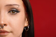 © New Africa - Woman with eyebrow and nose piercings on red background, closeup. Space for text