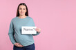 © New Africa - Pregnant woman holding card with word Name and question mark on pink background, space for text