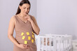 © New Africa - Thoughtful pregnant woman with notes with different names on her belly indoors, space for text