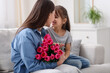 © New Africa - Happy Mother's Day. Little girl greeting her mom with beautiful flowers on sofa indoors