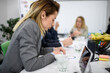 © Nikola Spasenoski - Business meeting in office with people discussing tasks and projects while focusing on laptops, paperwork, and personal items on table in modern work environment