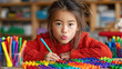 © Artsaba Family - A young girl is at her desk with colorful building blocks and markers, concentrating on her drawing as she engages in an art project in her classroom