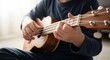 © Nataly - Child playing ukulele, focusing on hands strumming and fretting strings of small musical instrument. Learning playing ukulele develops creativity and musical skills.
