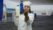 © Krakenimages.com - Woman chef in white uniform holding a glass milk bottle and hand pointing toward camera under a building canopy, smiling; freshness trust joy.