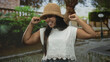 © Krakenimages.com - Hispanic woman raises fists and laughs on a street, wearing a straw hat and white lace blouse beside a cobblestone walkway and lamp post; joy celebration.