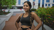 © Krakenimages.com - Sporty woman posing hands on hips showing midriff and sportsbra in front of building steps and planters; confidence motivation wellness.