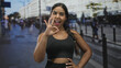 © Krakenimages.com - Sporty hispanic woman shows ok hand gesture while smiling with visible midriff on a busy street; confidence energy.