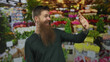 © Krakenimages.com - Man with long red beard gestures with open palms and excited grin at colorful flower market stall; joy.