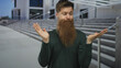 © Krakenimages.com - Young man with long beard raises hands in shrug on concrete city street building facade; uncertainty.