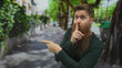 © Krakenimages.com - Bearded man pointing with finger and finger to lips for silence on sunny green city street; quiet secrecy mystery.