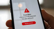 © Rakin - A hand holds a smartphone displaying a red 'Fraud Alert' with warning sign, unusual activity detected.