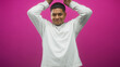 © Krakenimages.com - Hispanic man with beard raising hands above head and smiling in studio pink backdrop wearing white long sleeve shirt and visible face; playful confidence.