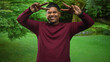 © Krakenimages.com - Hispanic man with beard smiling and making peace sign with hands wearing maroon shirt in forest; playful joy.