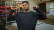 © Krakenimages.com - Hispanic man with beard showing thumbs pointing to chest in front of stacked thread spools and fabric table in a sewing studio; confidence craftsmanship.