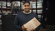© Krakenimages.com - Man holding a paper bag with both hands and smiling while presenting a delivery inside a building; friendly service.