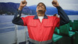 © Krakenimages.com - Man in red work uniform points both index fingers upward on a ferry deck with green passenger seats and mountainous shoreline building visible; triumph.