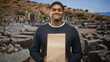 © Krakenimages.com - Hispanic man with beard holding a paper bag by both hands and smiling, facing forward in ancient ruins on street; amused curiosity.