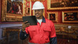 © Krakenimages.com - Man construction worker in hard hat and red uniform holding tablet and checking screen in museum gallery; inspection duty.