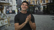 © Krakenimages.com - Man clapping hands on street corner while smiling broadly in urban setting and wearing a black t shirt; joy.