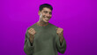 © Krakenimages.com - Man pumps fists wearing a green sweater with a beaming grin and closed eyes in purple studio; excitement.
