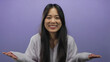© Krakenimages.com - Young chinese woman smiling playfully over isolated purple background, conveying a sense of joy with long black hair and light gray sweater.