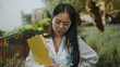© Krakenimages.com - Young chinese woman doctor in uniform holding a clipboard with stethoscope standing thoughtfully in a picturesque green park setting during daylight outdoors.