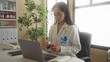 © Krakenimages.com - Woman doctor examines medicine bottle in a clinic, highlighting her focus in a hospital setting, with a laptop and stethoscope on the desk, showcasing a professional environment.